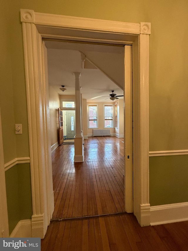 hall featuring decorative columns, radiator, and hardwood / wood-style floors