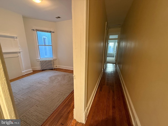 corridor with dark wood-type flooring and radiator heating unit