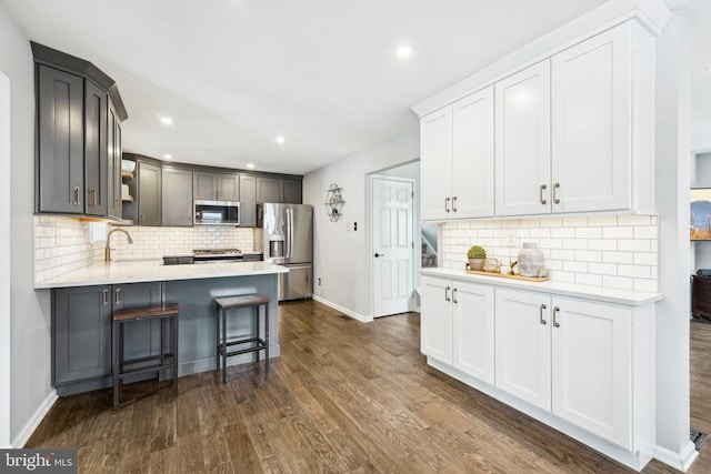 kitchen with dark wood-type flooring, stainless steel appliances, white cabinets, a kitchen bar, and decorative backsplash