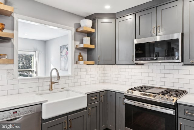 kitchen featuring sink, gray cabinets, stainless steel appliances, tasteful backsplash, and light stone countertops