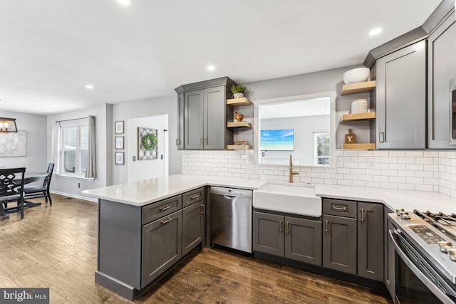 kitchen with tasteful backsplash, sink, kitchen peninsula, stainless steel appliances, and dark wood-type flooring