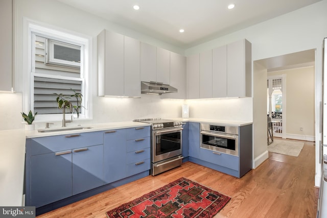 kitchen featuring blue cabinets, sink, white cabinets, stainless steel appliances, and light hardwood / wood-style flooring