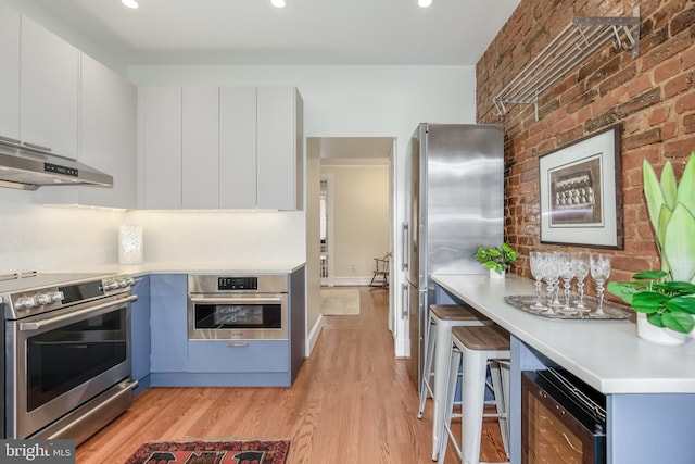 kitchen with appliances with stainless steel finishes, a kitchen breakfast bar, light hardwood / wood-style floors, white cabinets, and brick wall