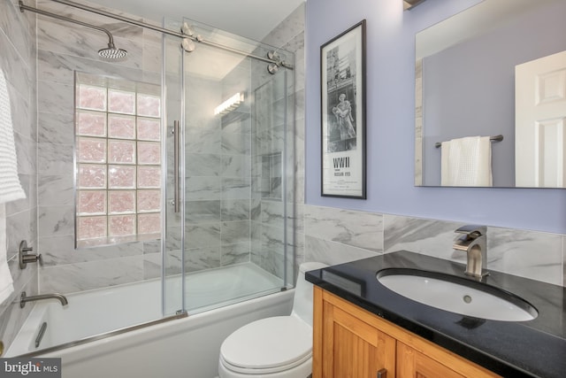 full bathroom featuring shower / bath combination with glass door, vanity, toilet, and tile walls