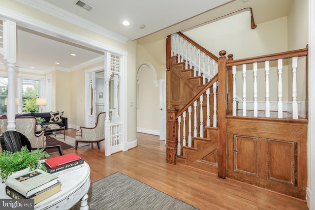 foyer entrance featuring hardwood / wood-style flooring, crown molding, and ornate columns