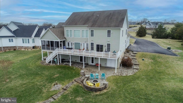 rear view of property with a deck, a yard, an outdoor fire pit, a sunroom, and a patio area