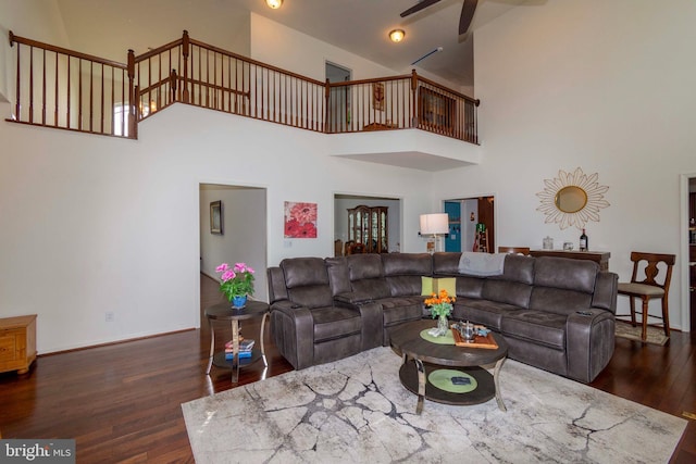 living room with dark wood-type flooring, ceiling fan, and a high ceiling