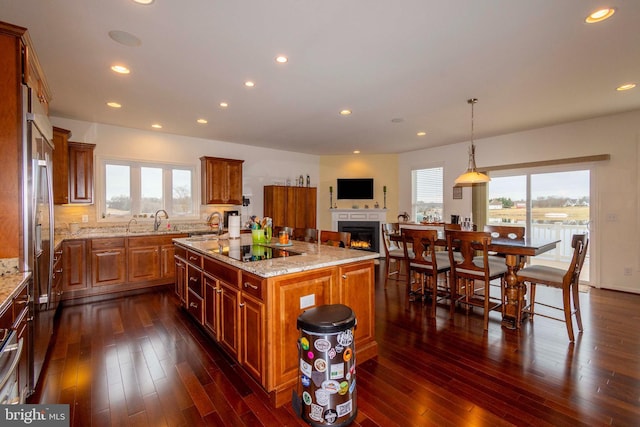 kitchen featuring sink, light stone counters, a center island, black electric cooktop, and pendant lighting