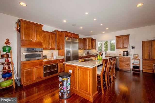 kitchen with a breakfast bar, stainless steel appliances, light stone countertops, a kitchen island, and dark hardwood / wood-style flooring