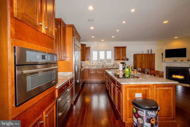 kitchen featuring appliances with stainless steel finishes, sink, dark hardwood / wood-style flooring, a kitchen island with sink, and light stone counters