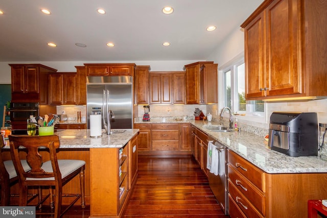 kitchen featuring sink, appliances with stainless steel finishes, dark hardwood / wood-style floors, a kitchen island, and light stone countertops