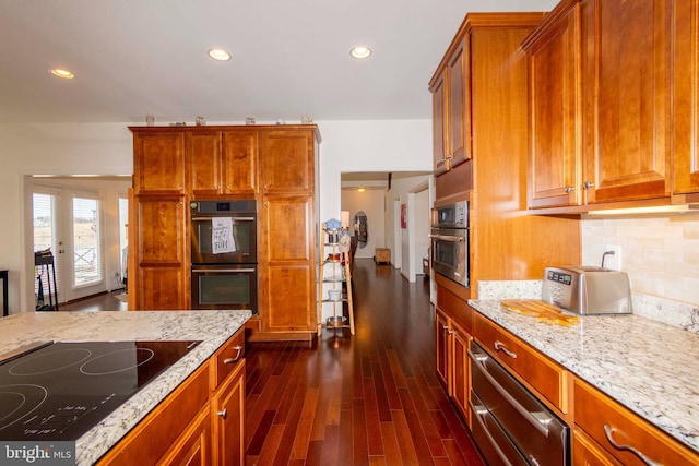 kitchen featuring light stone countertops, dark wood-type flooring, backsplash, and black appliances