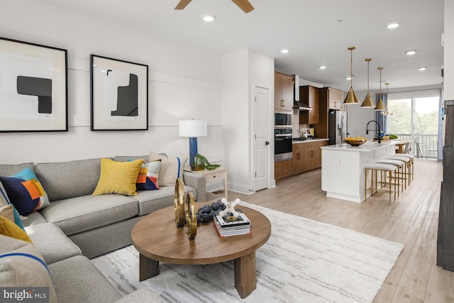 living room with light wood-type flooring, ceiling fan, and sink