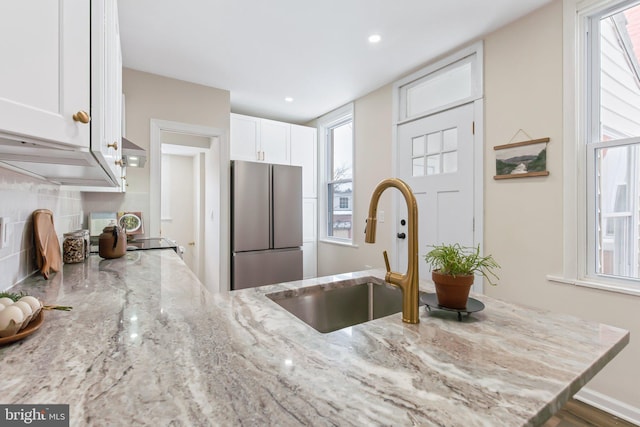 kitchen with sink, white cabinetry, tasteful backsplash, light stone counters, and stainless steel fridge