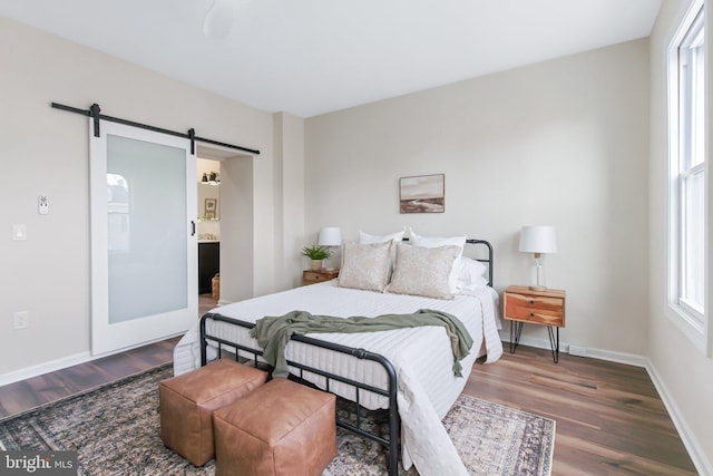 bedroom featuring hardwood / wood-style flooring, ensuite bath, a barn door, and multiple windows