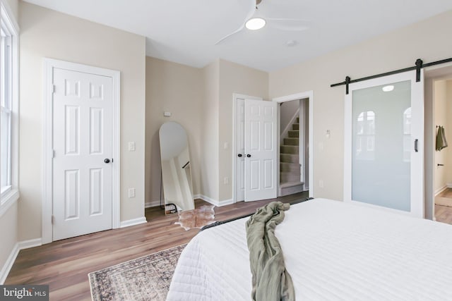 bedroom featuring hardwood / wood-style flooring, ceiling fan, a barn door, and ensuite bath