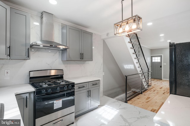 kitchen featuring black refrigerator, decorative light fixtures, gas stove, wall chimney exhaust hood, and gray cabinets