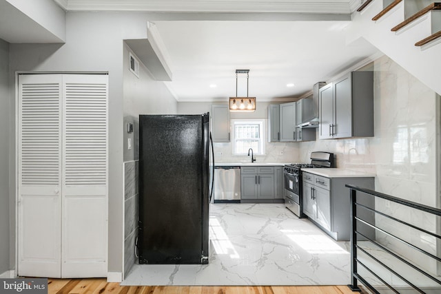 kitchen with appliances with stainless steel finishes, decorative light fixtures, tasteful backsplash, gray cabinetry, and wall chimney range hood