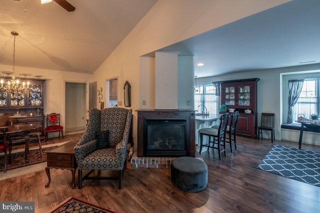 living room with ceiling fan with notable chandelier, a healthy amount of sunlight, dark hardwood / wood-style floors, and vaulted ceiling