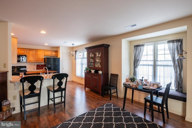 kitchen with dark wood-type flooring, a breakfast bar, tasteful backsplash, and black appliances