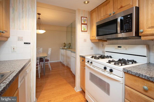 kitchen with pendant lighting, white appliances, tasteful backsplash, dark stone counters, and light wood-type flooring