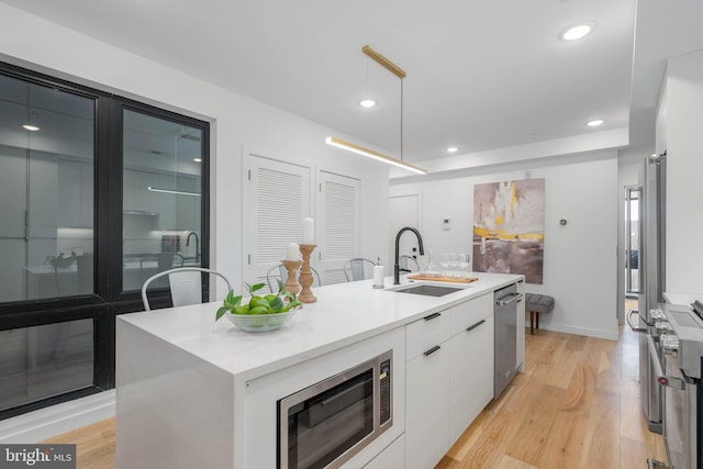 kitchen with white cabinets, light wood-type flooring, sink, stainless steel appliances, and a center island with sink