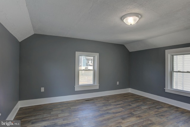 additional living space with a textured ceiling, dark hardwood / wood-style flooring, and lofted ceiling