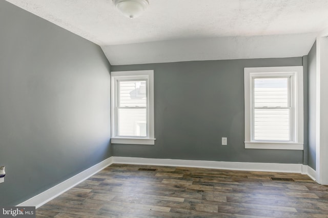 empty room with a wealth of natural light, dark hardwood / wood-style floors, lofted ceiling, and a textured ceiling