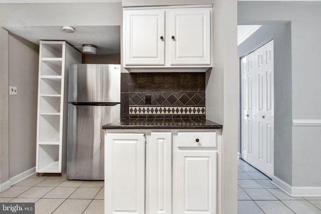 kitchen with tasteful backsplash, white cabinets, stainless steel fridge, dark stone counters, and light tile patterned floors