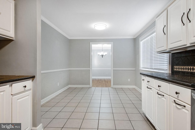 kitchen featuring dark stone countertops, white cabinets, a chandelier, light tile patterned floors, and crown molding