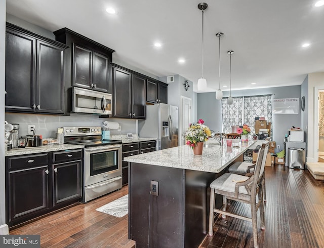 kitchen featuring appliances with stainless steel finishes, decorative light fixtures, a breakfast bar area, dark hardwood / wood-style flooring, and a center island with sink