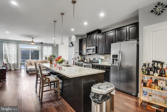 kitchen with appliances with stainless steel finishes, decorative light fixtures, an island with sink, a breakfast bar area, and light stone counters