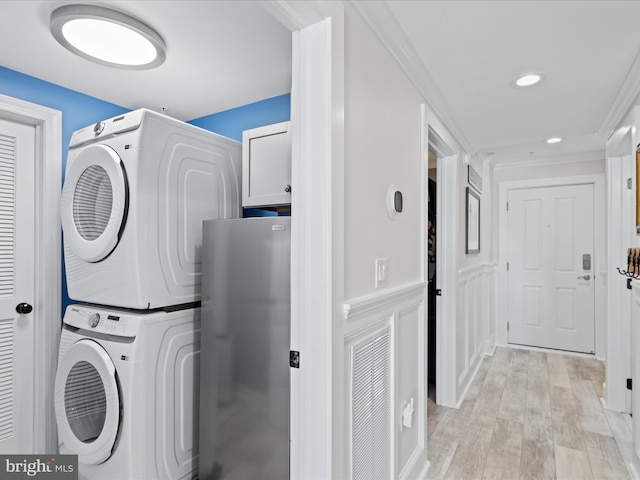 clothes washing area with cabinets, stacked washer and clothes dryer, and light wood-type flooring