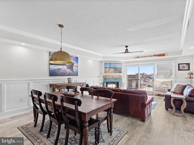 dining room featuring a textured ceiling, a brick fireplace, light hardwood / wood-style flooring, and a tray ceiling