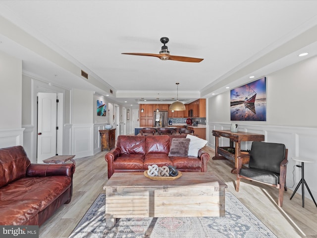 living room with ceiling fan, light hardwood / wood-style flooring, crown molding, and a tray ceiling