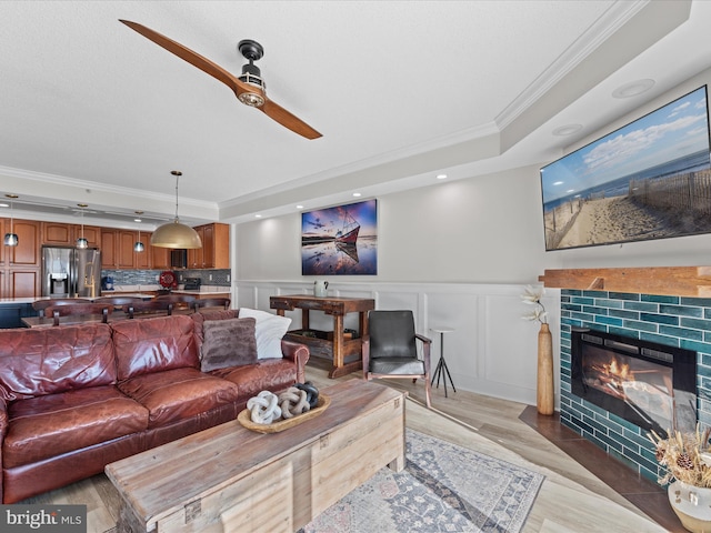 living room with ceiling fan, a tray ceiling, a fireplace, hardwood / wood-style floors, and ornamental molding