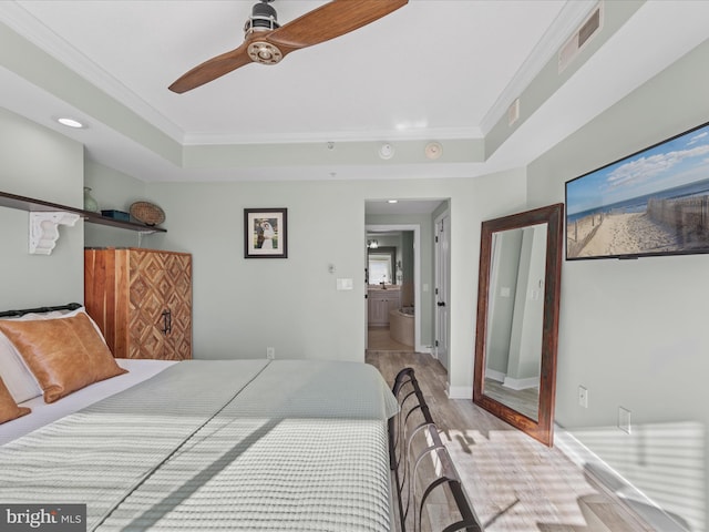 bedroom with light wood-type flooring, connected bathroom, a tray ceiling, and ceiling fan