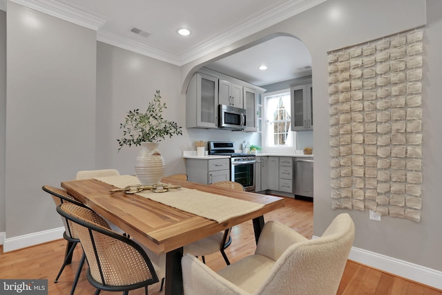 kitchen featuring stainless steel appliances, ornamental molding, gray cabinetry, and light wood-type flooring