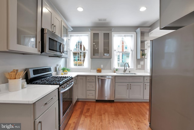 kitchen with stainless steel appliances, gray cabinets, sink, and light wood-type flooring