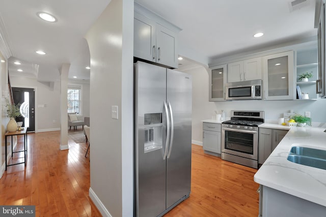 kitchen featuring gray cabinets, ornamental molding, appliances with stainless steel finishes, and light hardwood / wood-style floors