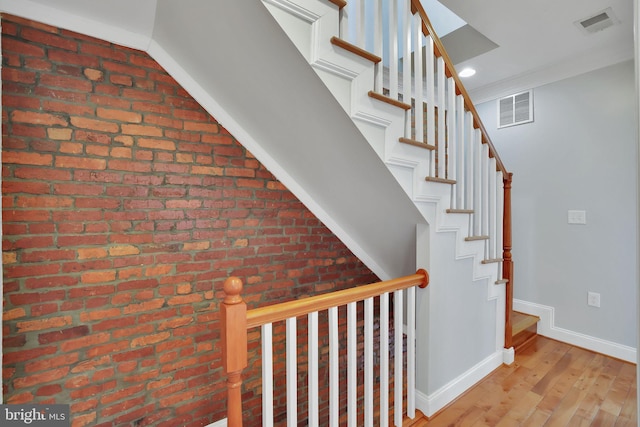 stairway with crown molding, brick wall, and hardwood / wood-style floors