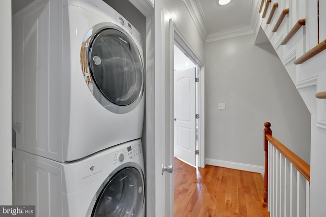 clothes washing area featuring stacked washer / drying machine, ornamental molding, and light hardwood / wood-style floors