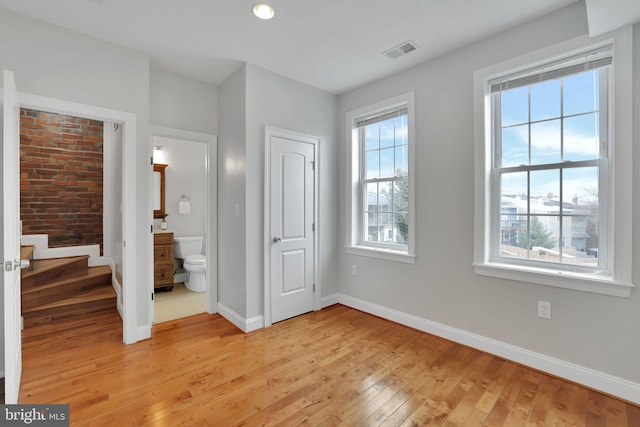 unfurnished bedroom with multiple windows, ensuite bathroom, and light wood-type flooring