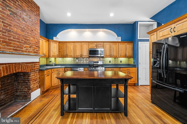 kitchen with appliances with stainless steel finishes, dark countertops, light wood-style flooring, and tasteful backsplash