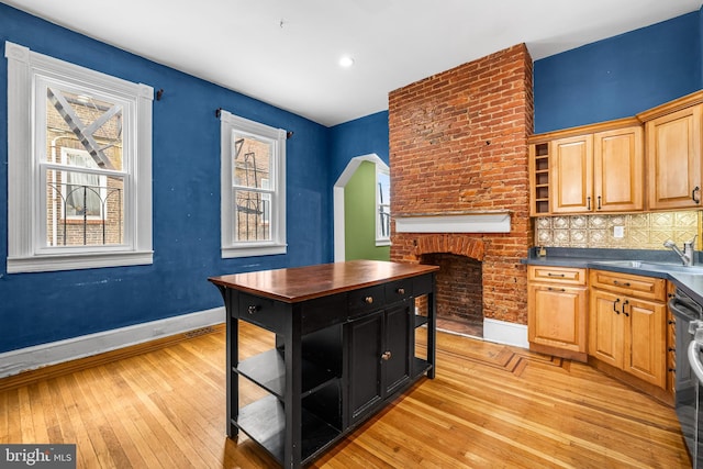 kitchen featuring tasteful backsplash, baseboards, light wood-type flooring, a fireplace, and a sink