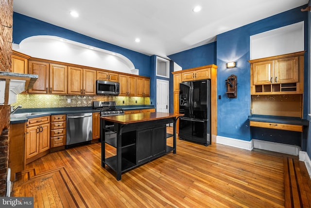 kitchen with wood-type flooring, stainless steel appliances, a sink, tasteful backsplash, and dark countertops