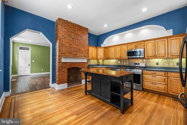 kitchen with arched walkways, dark countertops, light wood-style flooring, decorative backsplash, and appliances with stainless steel finishes