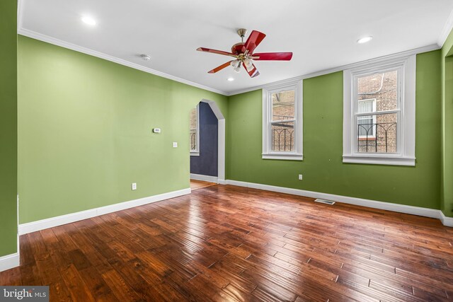 spare room featuring arched walkways, visible vents, baseboards, hardwood / wood-style floors, and crown molding