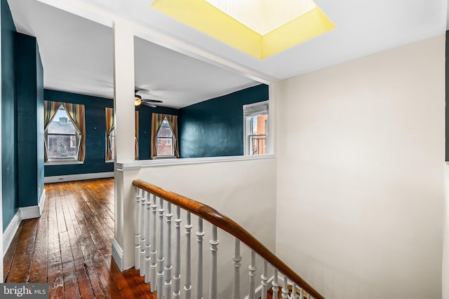 hallway featuring dark wood-style floors, baseboards, and an upstairs landing