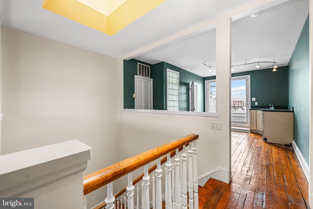 corridor featuring hardwood / wood-style flooring, a sink, an upstairs landing, baseboards, and track lighting